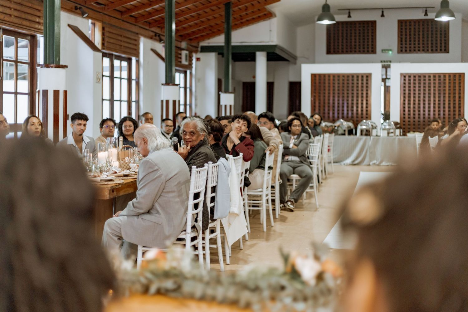 Reception guests are seated at elegant tables in a bright, modern event space with exposed wooden beams.