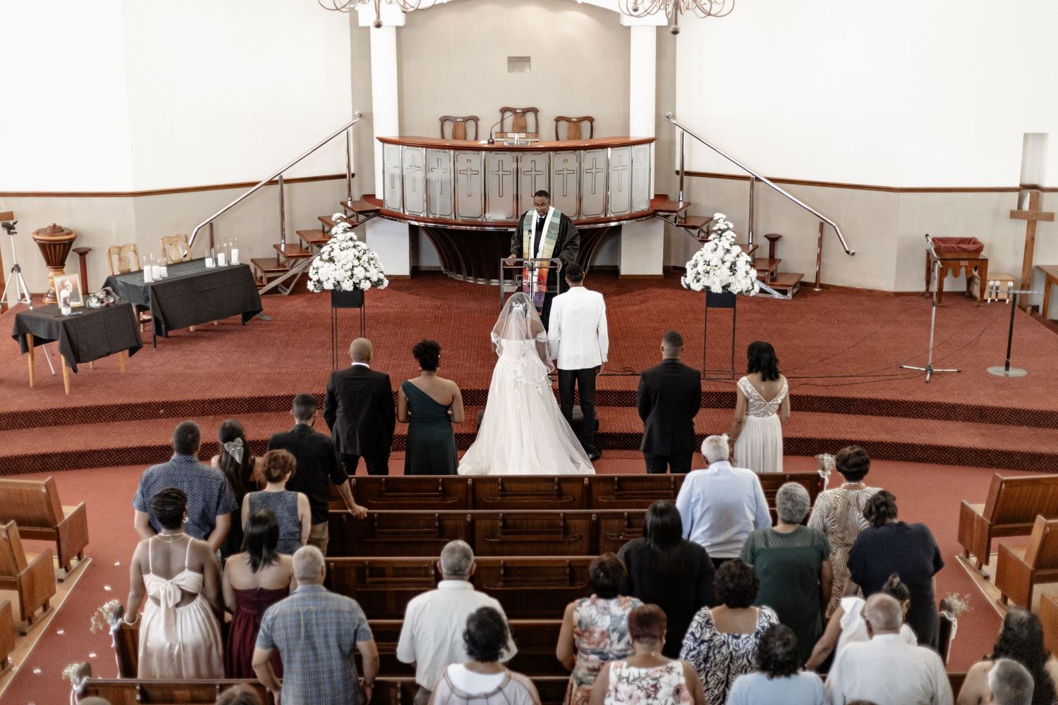 Wedding ceremony taking place in a traditional church sanctuary with red carpeted steps and guests observing from pews.