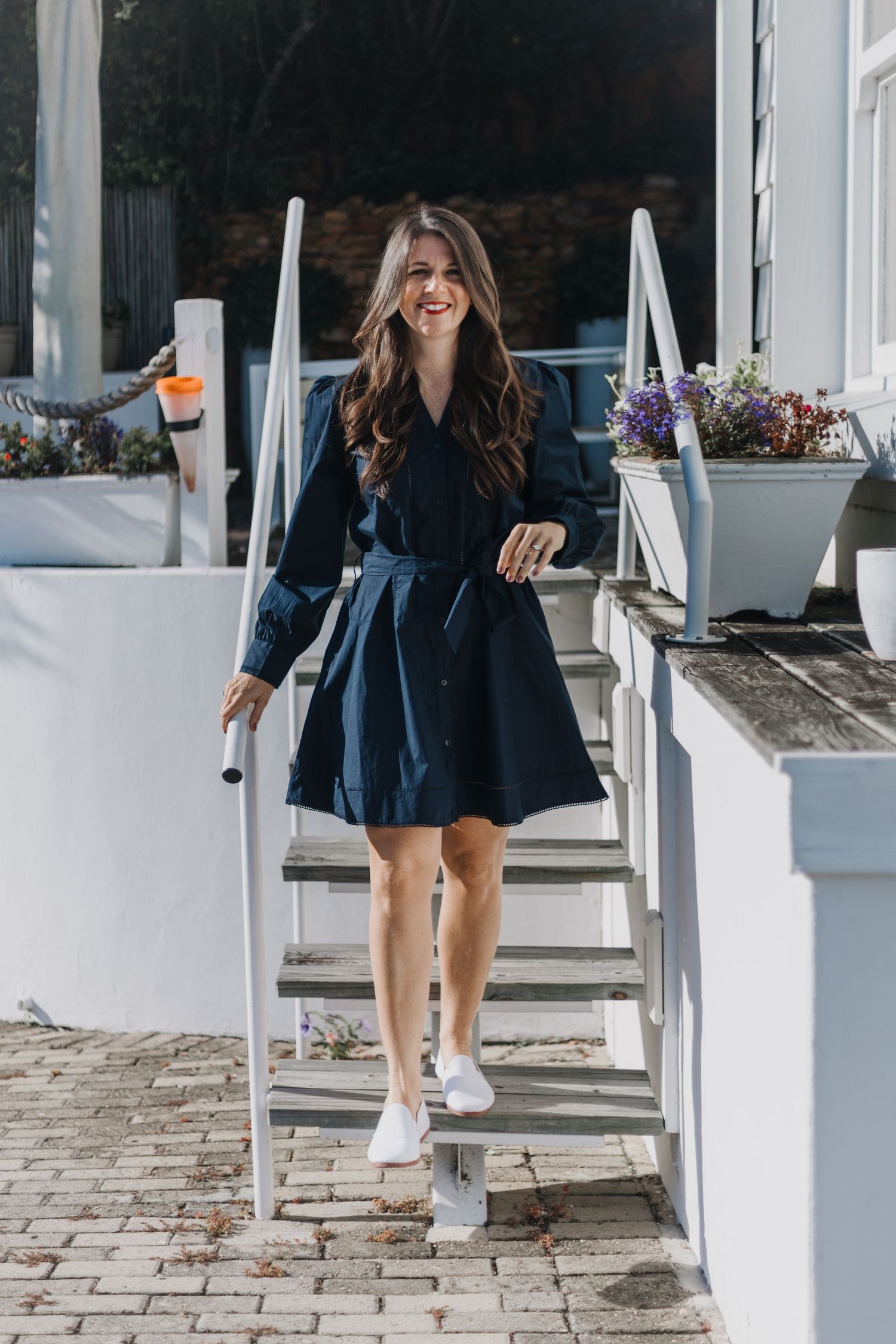 Navy dress and white sneakers outfit photographed on outdoor white stairs with floral planters.