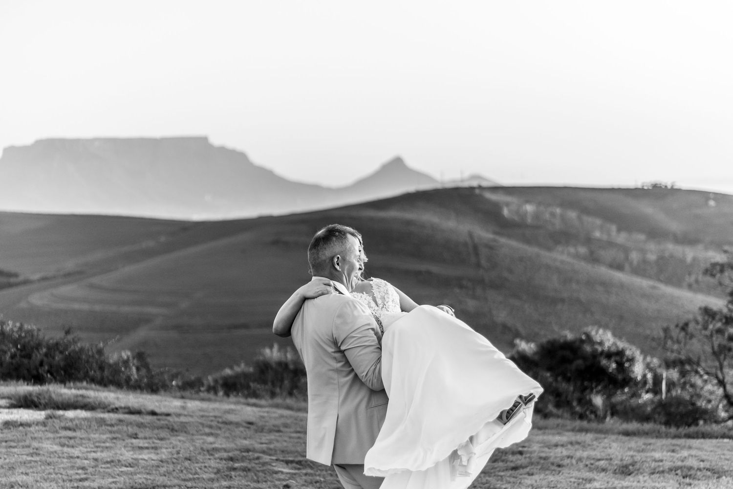 A romantic black and white wedding photo of a couple on a hilltop with misty mountains in the background.