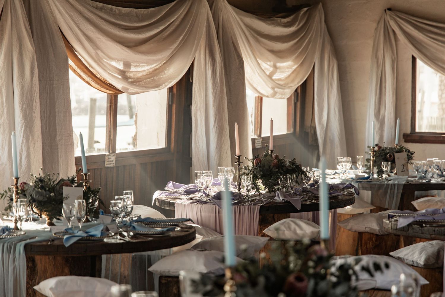 Elegant wedding reception venue with draped fabric decor, round tables, and romantic floral centerpieces.