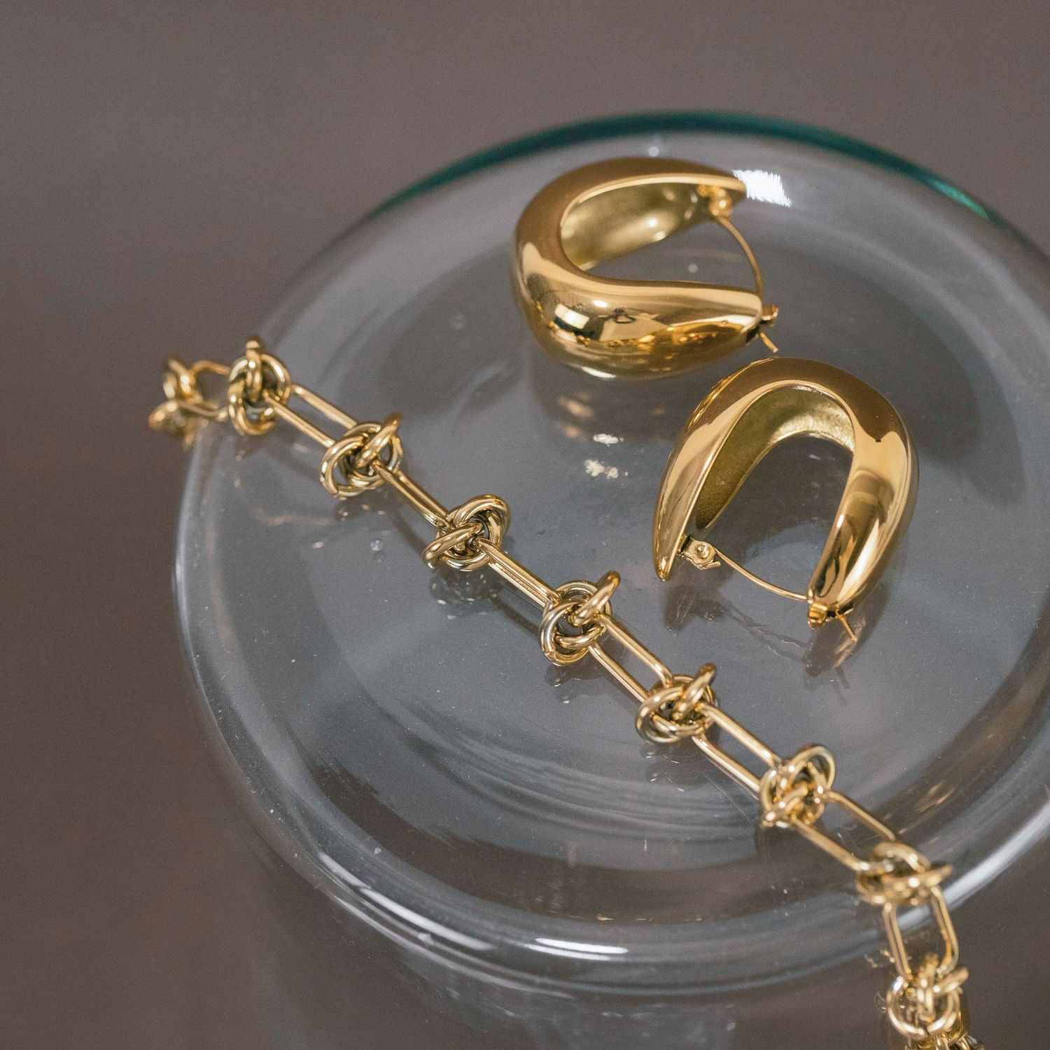 Delicate gold chain bracelet with connected geometric links displayed on a curved glass surface.