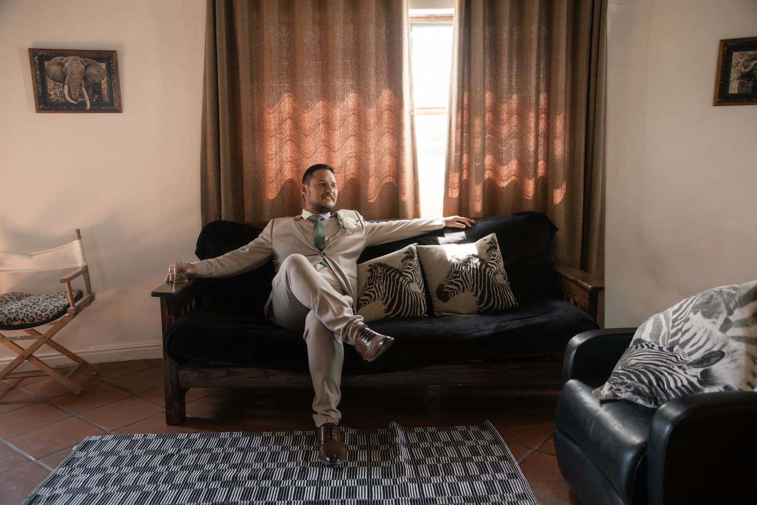 Man in suit relaxing on dark sofa in elegant room with curtained windows and decorative pillows.