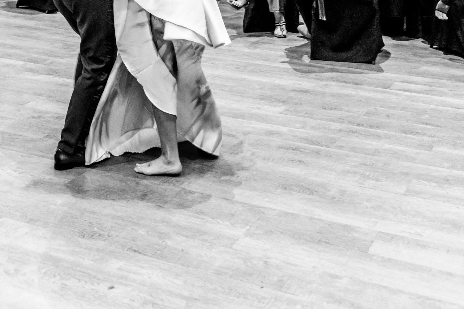 Dancers in flowing white dresses perform traditional ballet movements on a wooden dance floor during a performance.