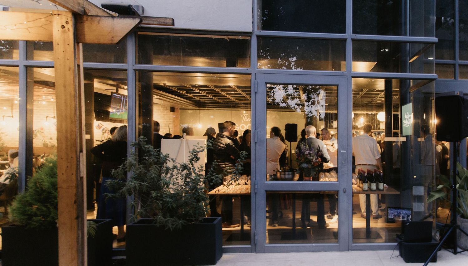 Modern restaurant exterior with glass windows and outdoor seating area illuminated at dusk.
