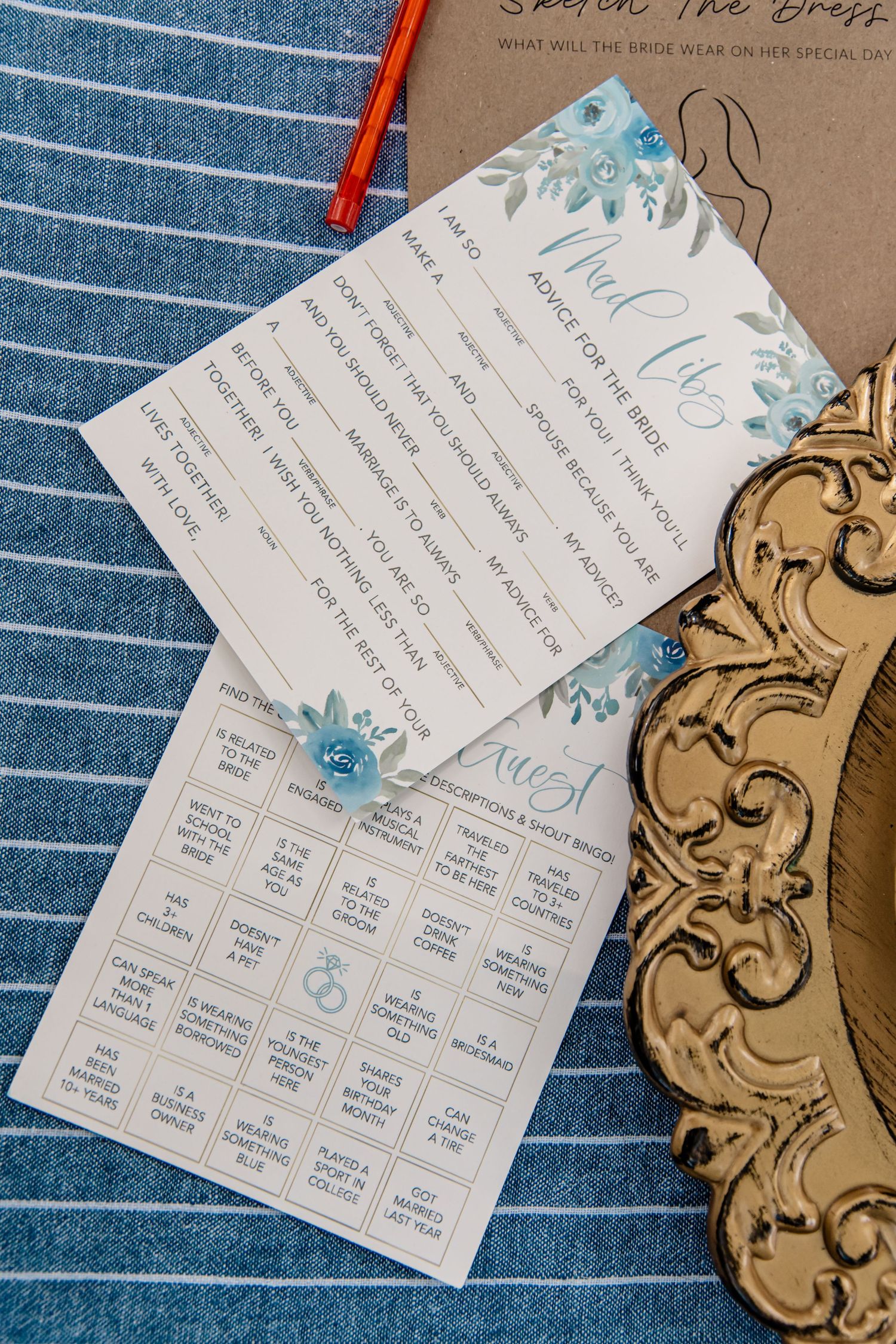 Bridal shower games including Mad Libs, advice cards, and bingo on blue striped fabric with gold tray.