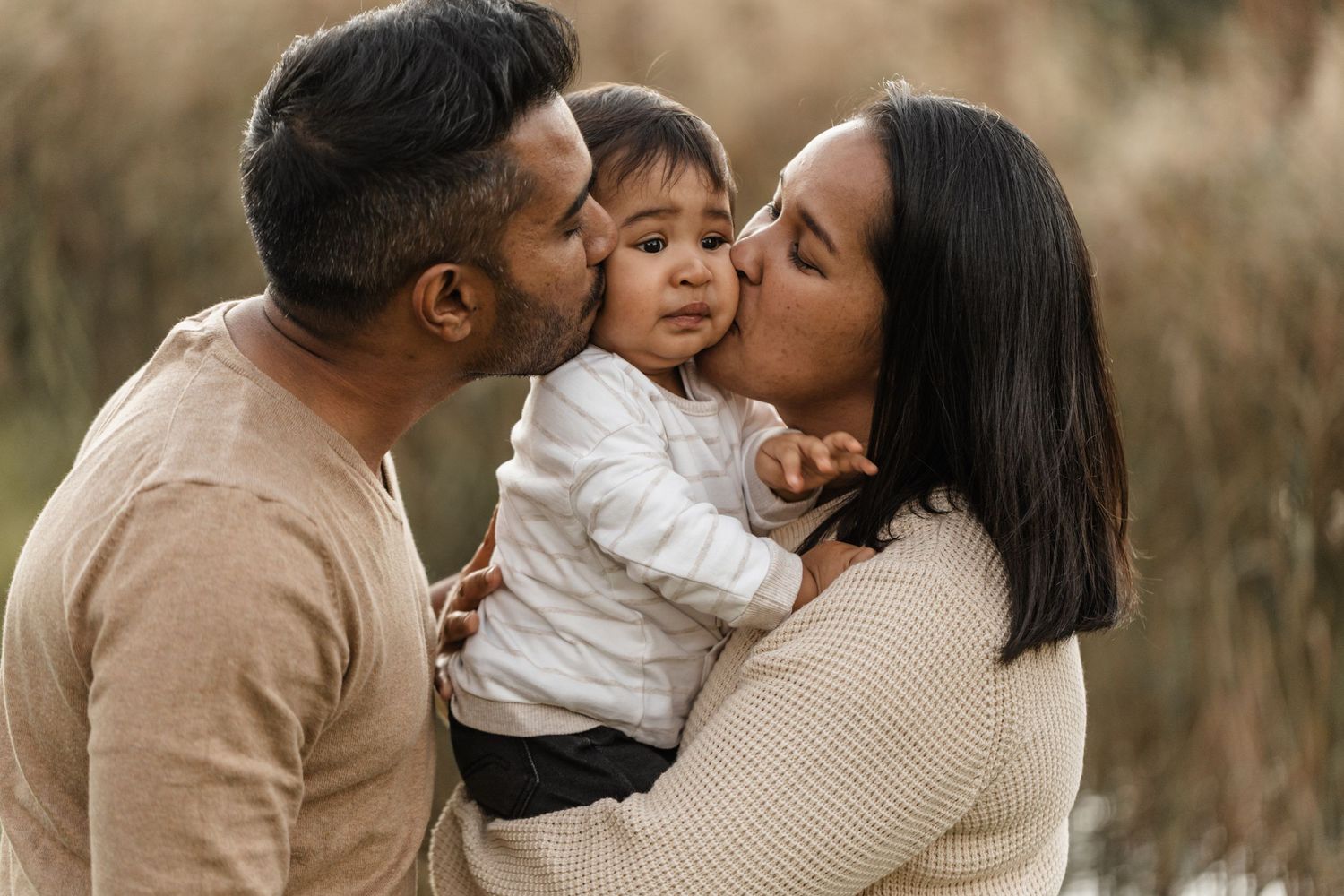 A loving family embraces and shares kisses in a golden field during sunset.