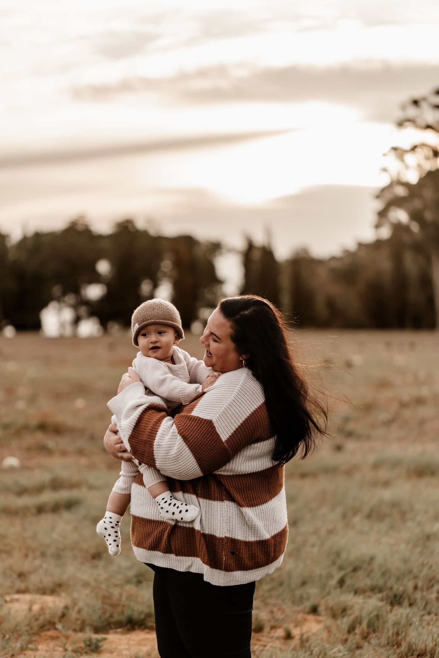 A parent and baby share a tender moment together in a golden field at sunset.