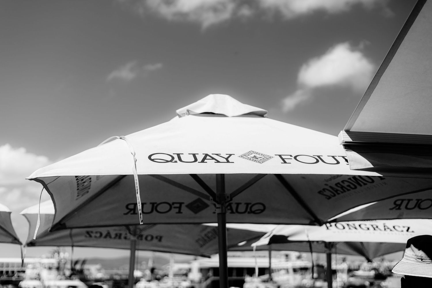 Outdoor patio umbrellas provide shade at a beachfront dining area with cloudy sky in the background.