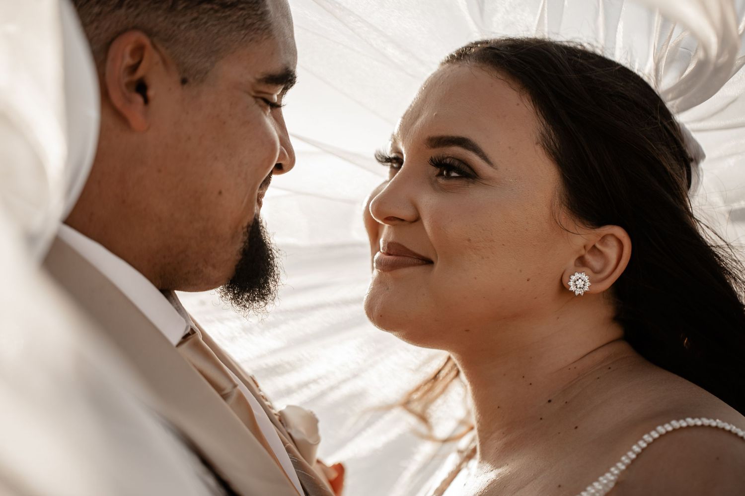 A tender romantic moment between newlyweds as they gaze at each other against a bright white background.