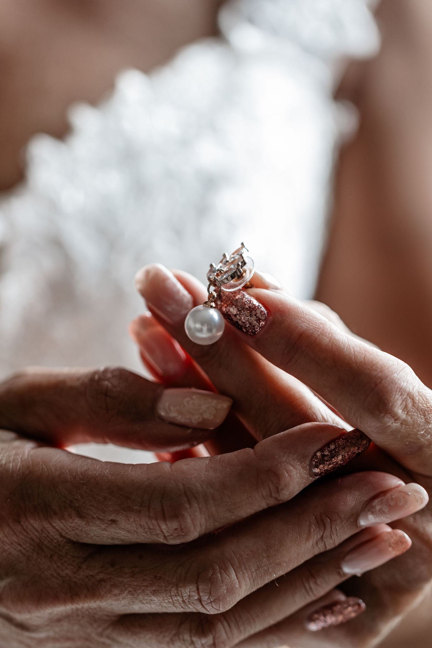Hands holding delicate pearl and diamond engagement ring with intricate details captured in soft lighting.