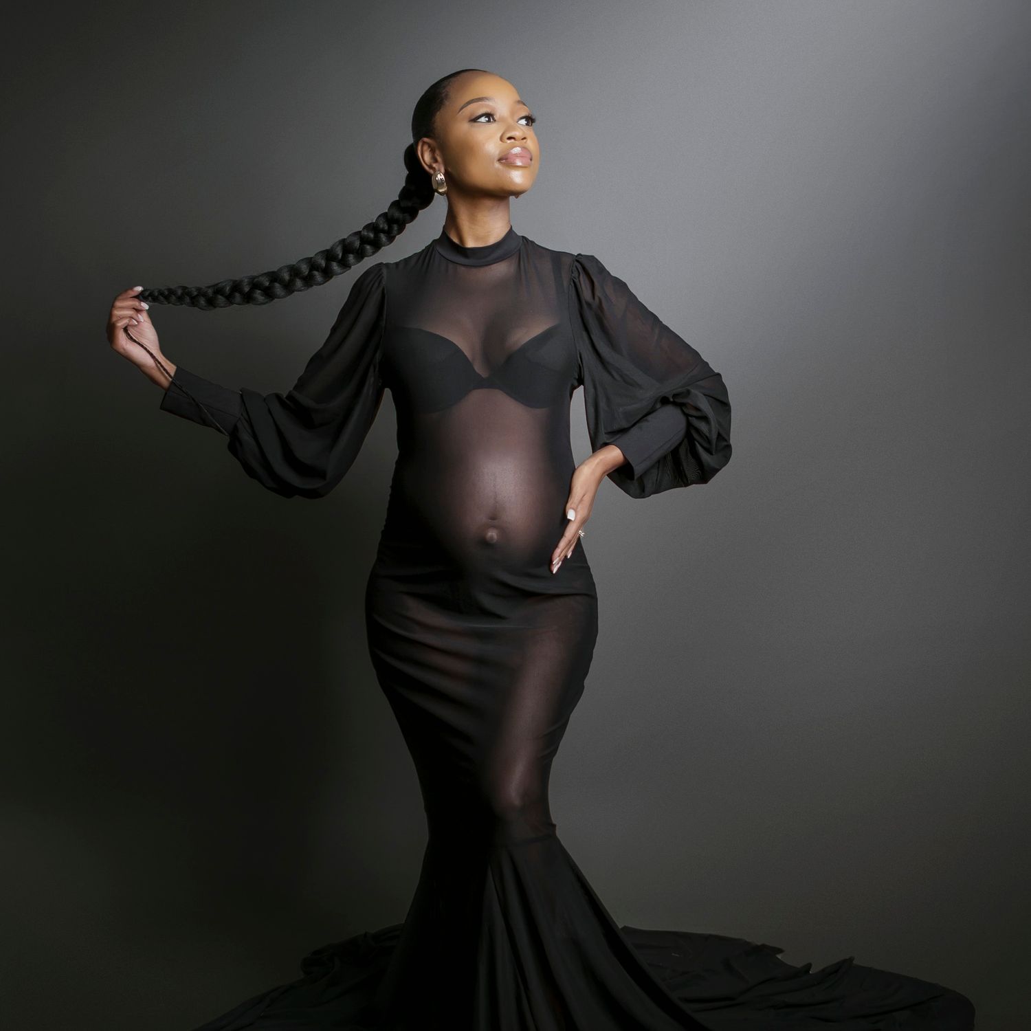 Studio portrait of a pregnant woman in a black mermaid dress holding her long braid.