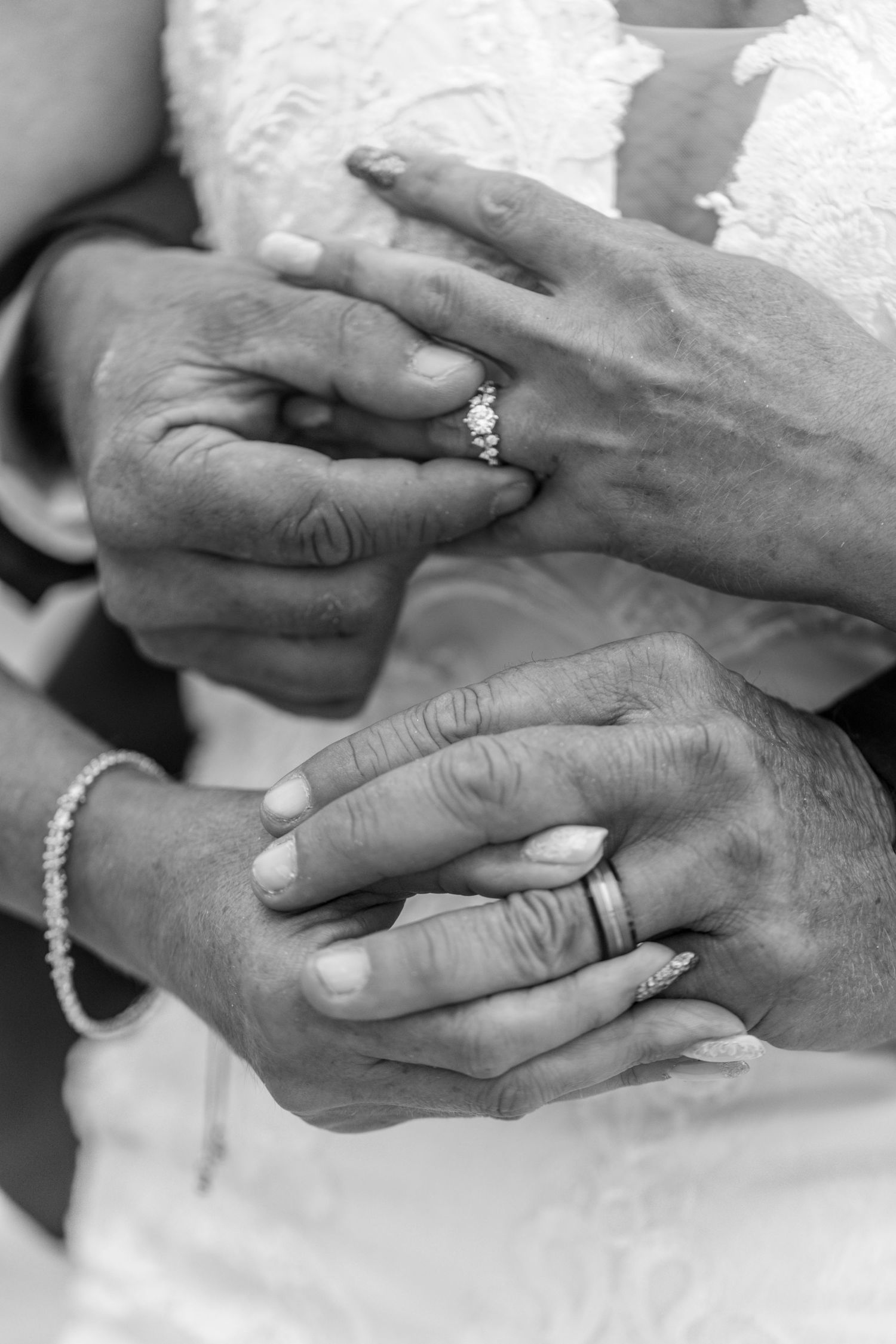 Black and white closeup of two hands displaying wedding rings during a marriage ceremony.