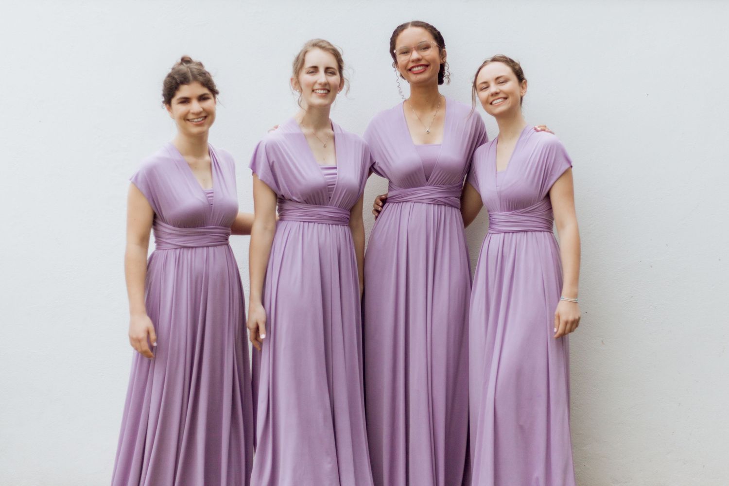 Four bridesmaids pose together wearing matching long lavender dresses with empire waists and cap sleeves.