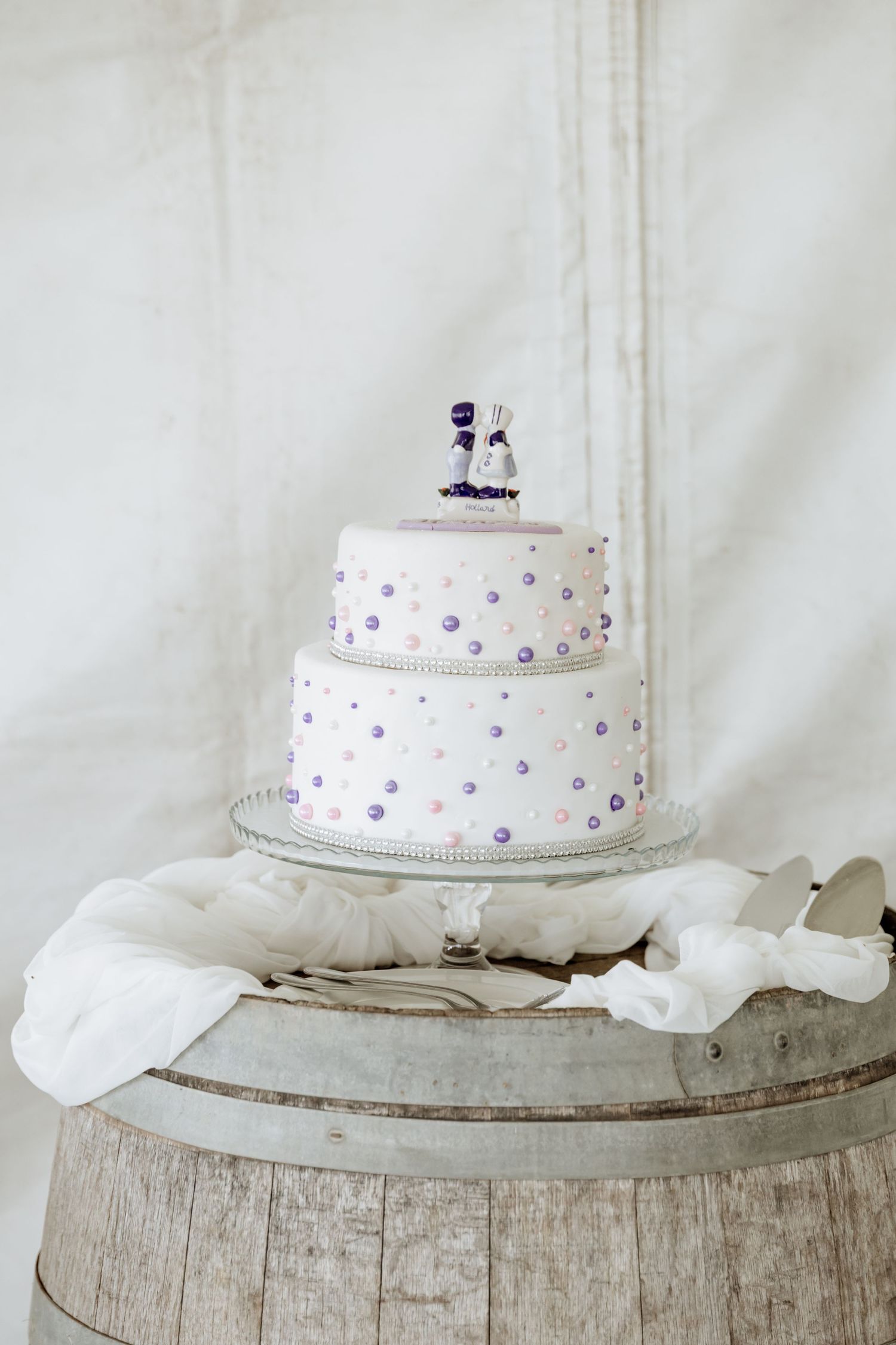 Three white wedding cakes with delicate purple polka dot decorations sit atop rustic wooden platforms.