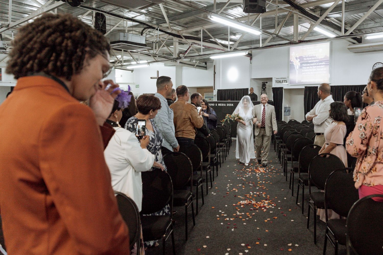 Group of people seated at long tables in a bright industrial-style space during what appears to be a workshop or conference event.