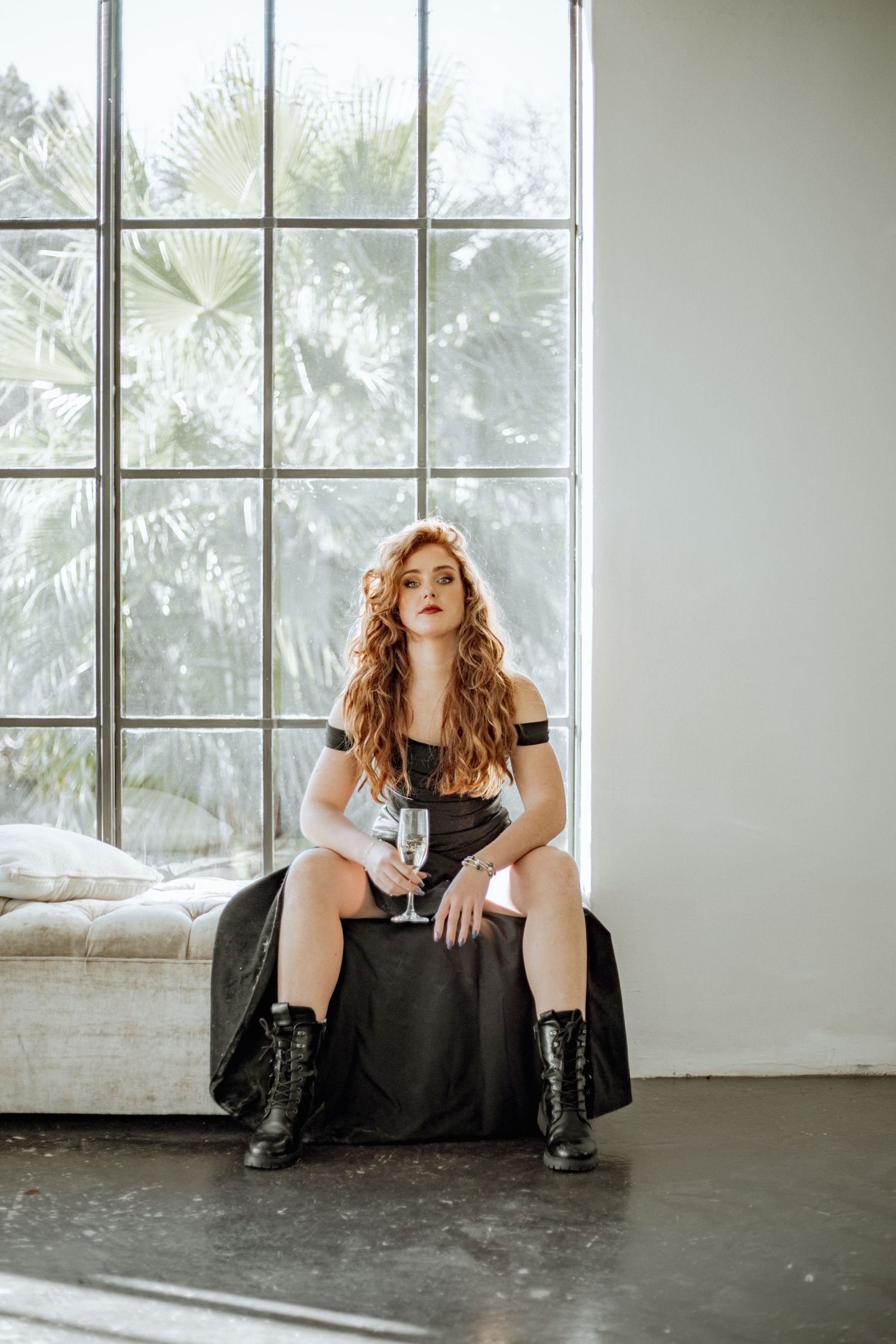 Artistic triptych portrait showing seated figure in black dress against light-filled industrial space.