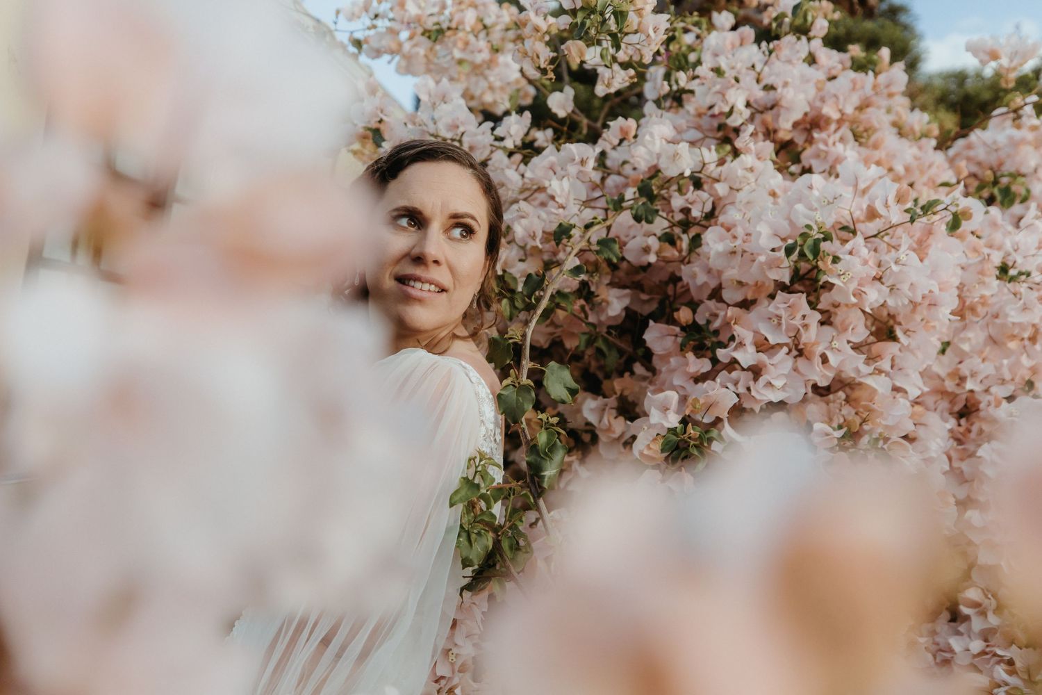 Dreamy spring portrait surrounded by blooming pink cherry blossoms in soft natural lighting.