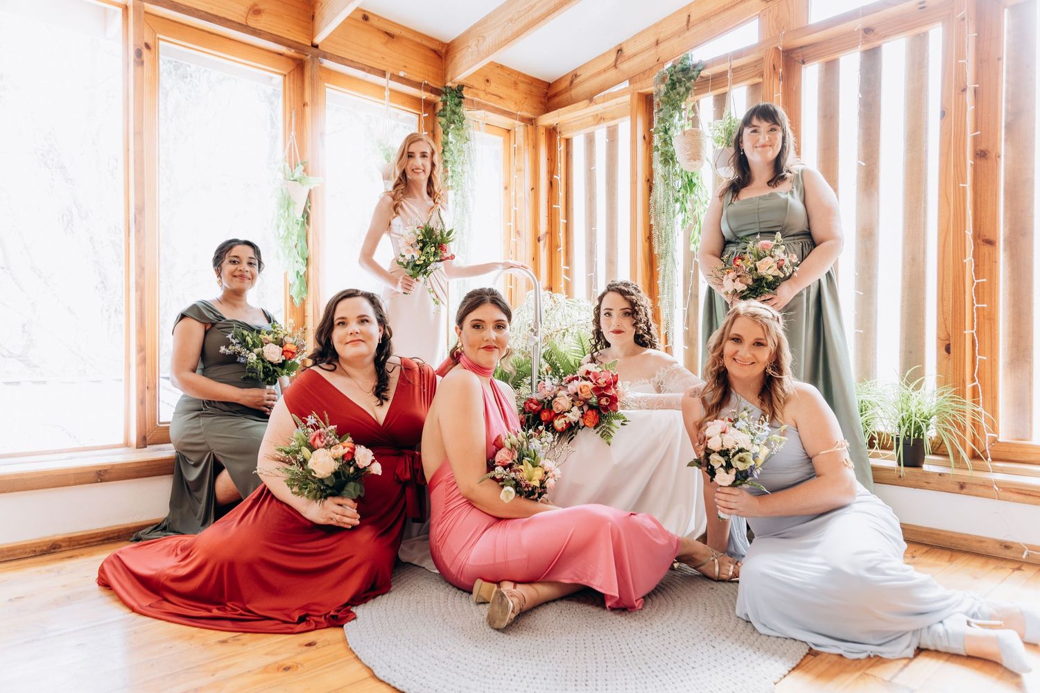 Bride and bridesmaids in colorful dresses posing with bouquets in a bright wooden venue.