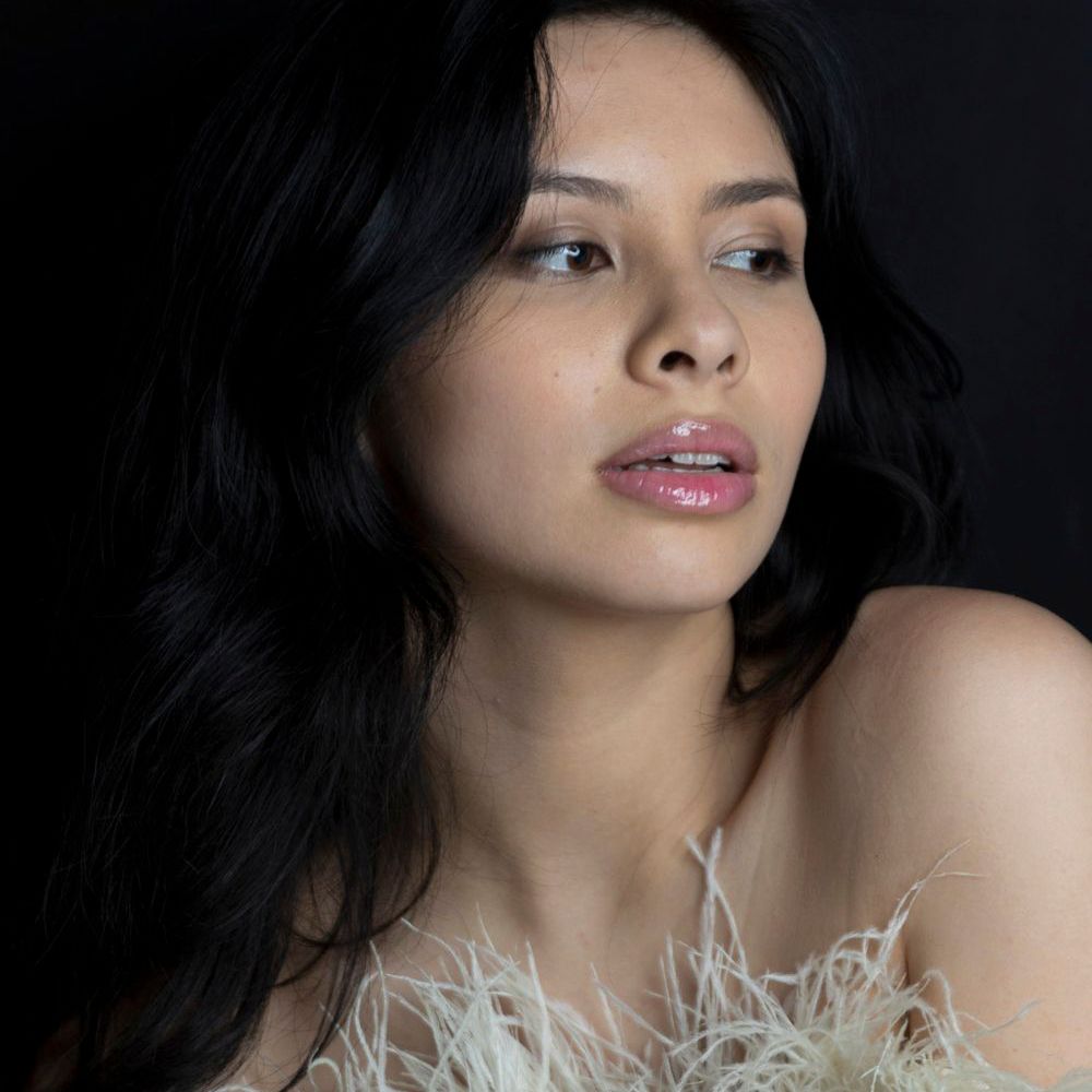 Glamour beauty shot with red lips and feathered white dress against dark backdrop.