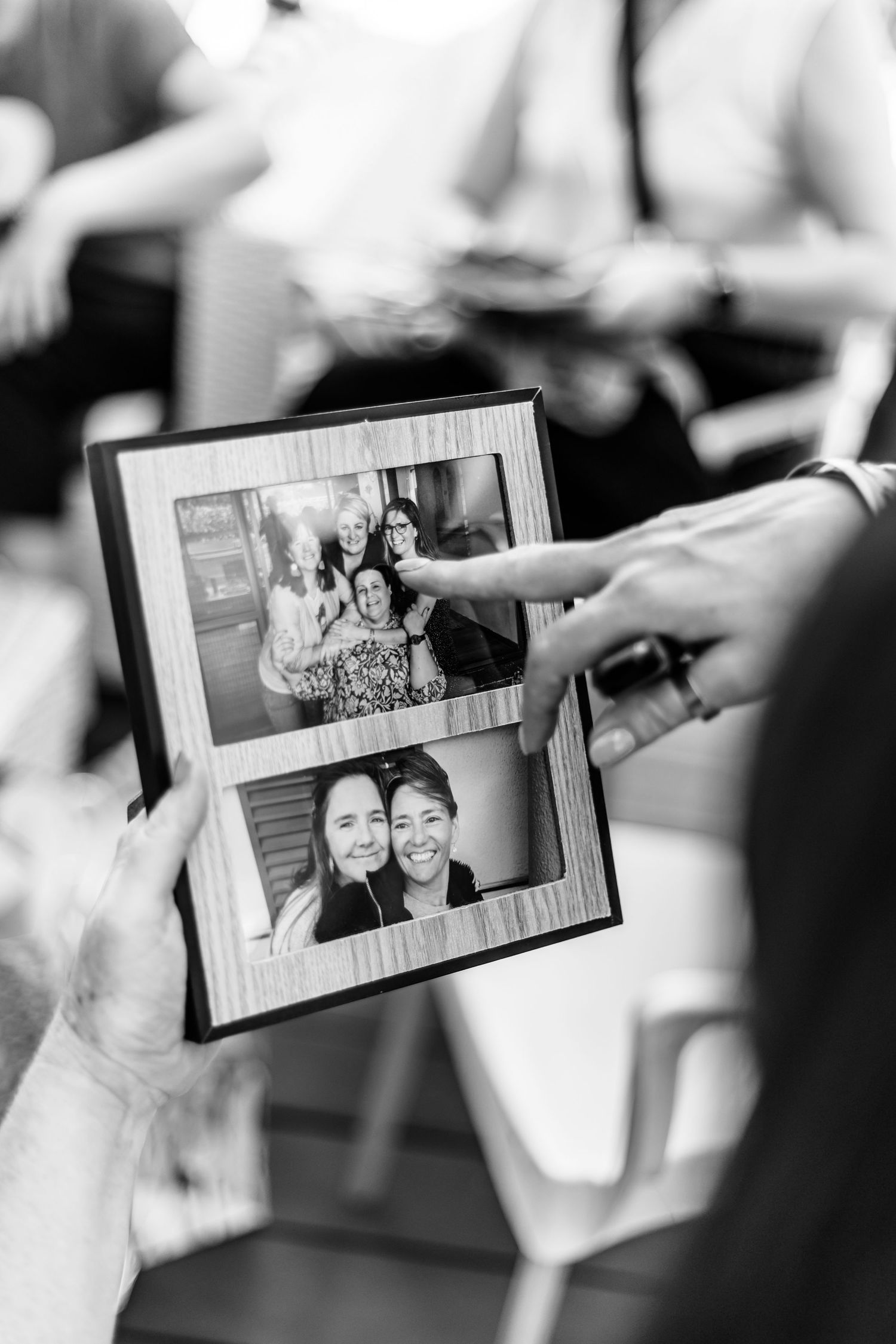 Black and white photo showing hands pointing at framed photographs in a casual setting.
