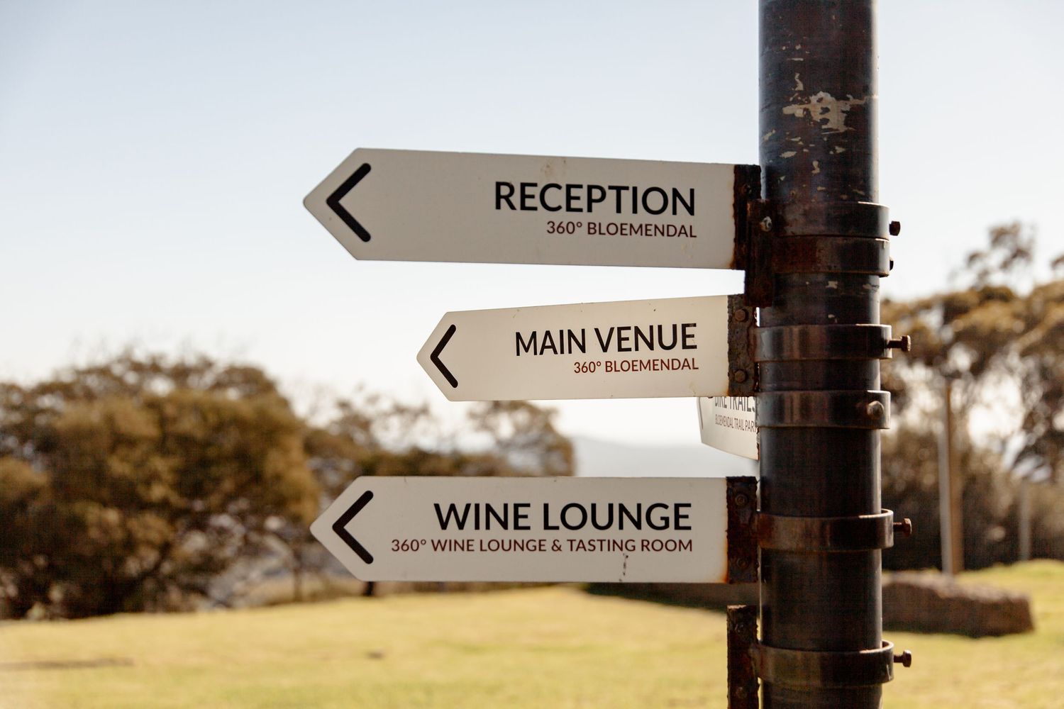 Wedding venue directional signs mounted on wood post pointing to reception, wine lounge and main venue areas.