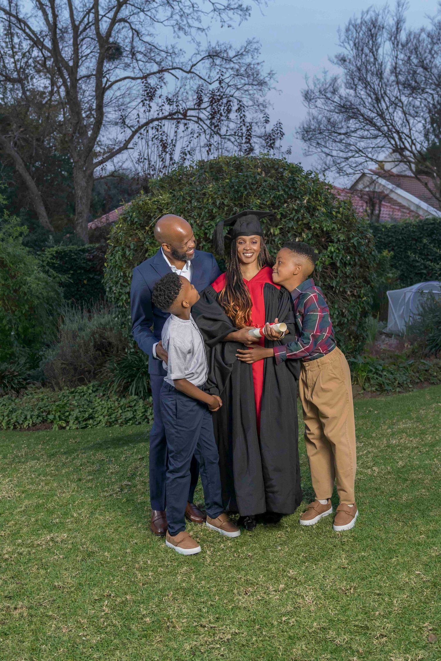 A family celebrates a graduation in a garden setting on a cloudy day, standing together on the grass.