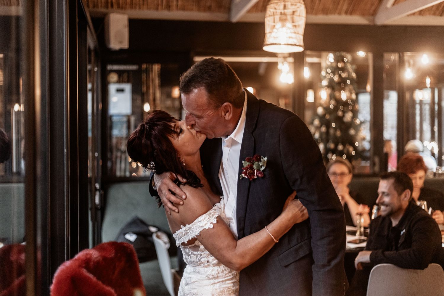 Couple embraces during romantic candlelit dance at elegant rustic wedding reception with string lights and wooden beams.