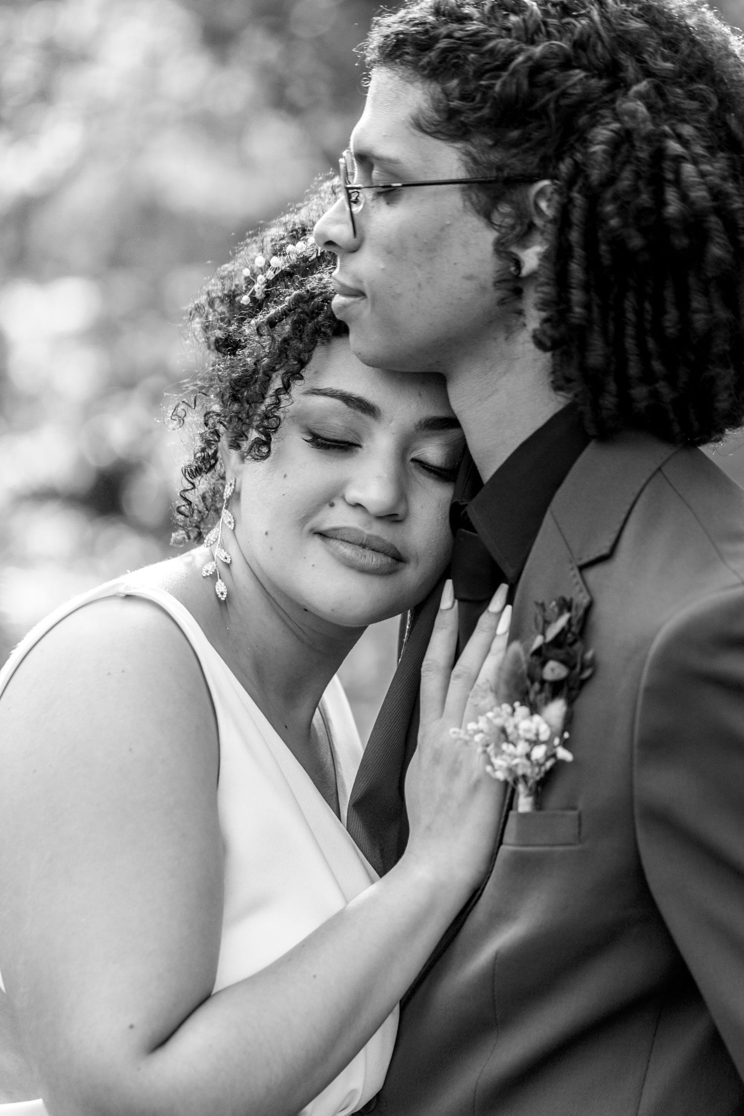 A tender black and white wedding portrait showing a couple in an intimate moment with the bride in white and groom in suit.