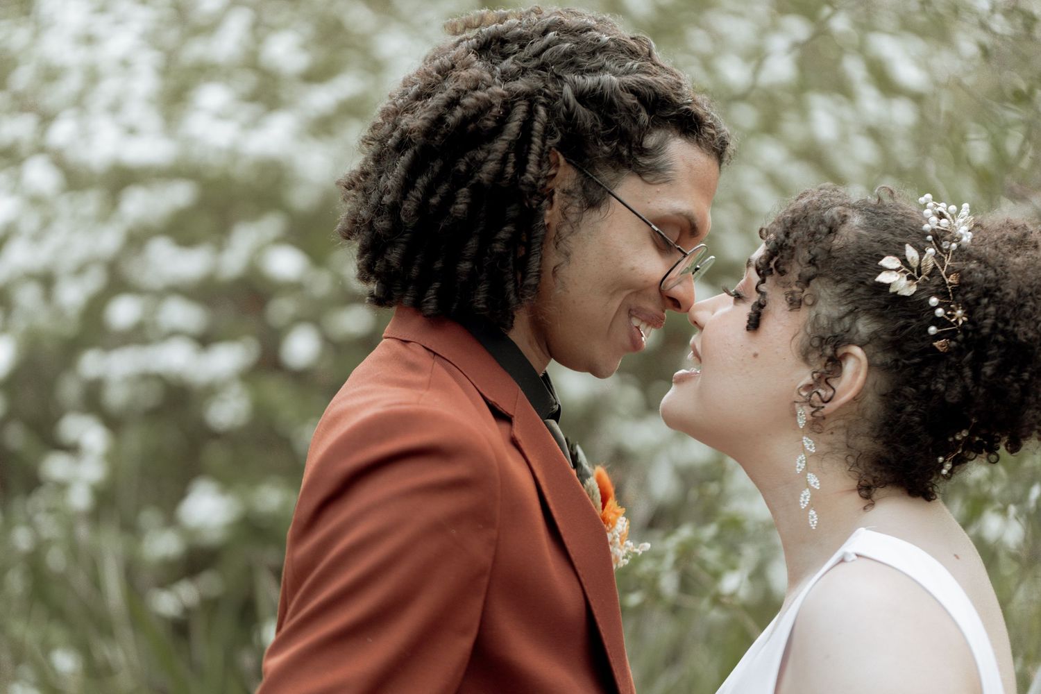 Couple shares intimate moments against natural outdoor backdrop with white flowering trees in spring.