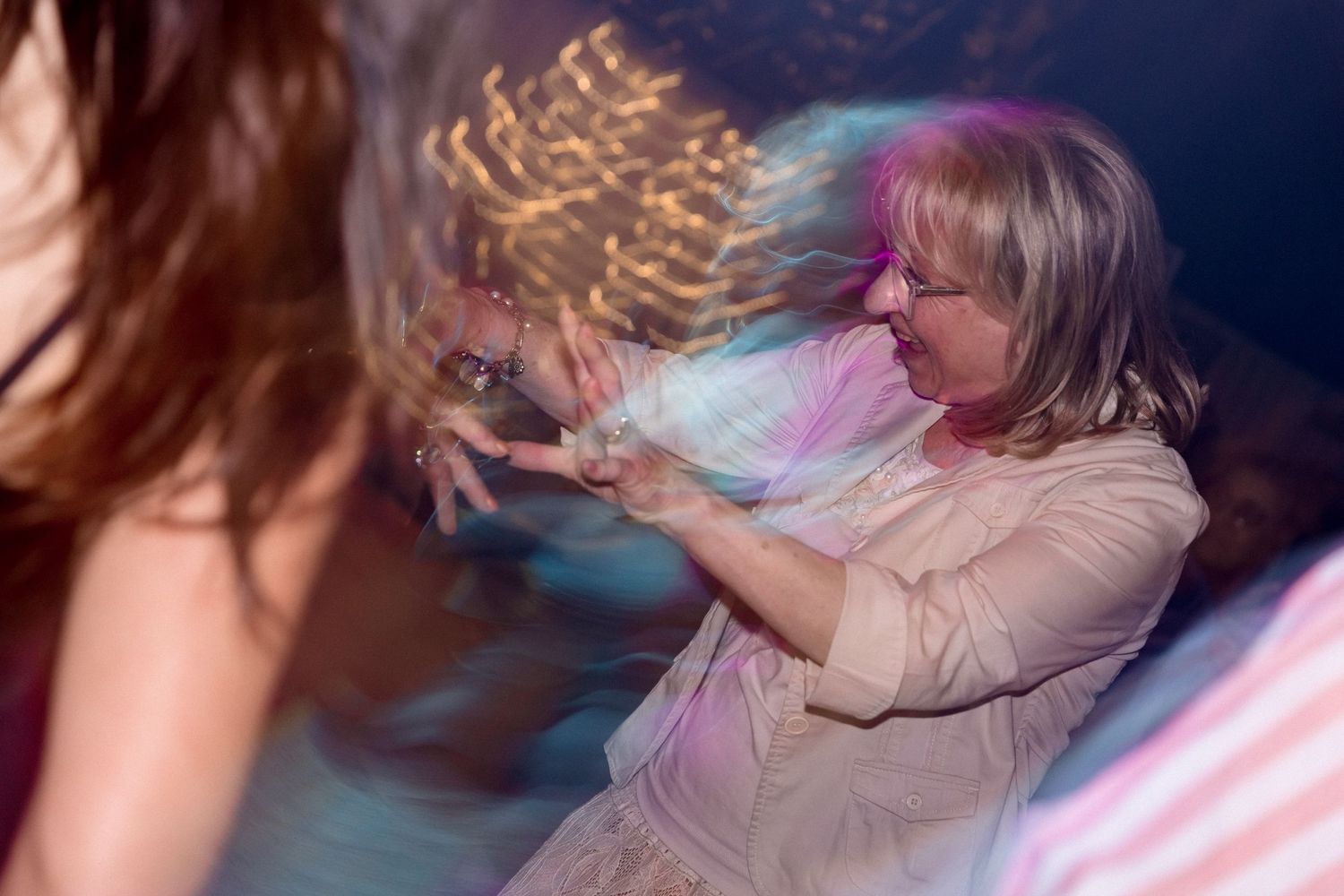 A person with long hair dances and spins in a flowing dress under colorful lights at a party or celebration.