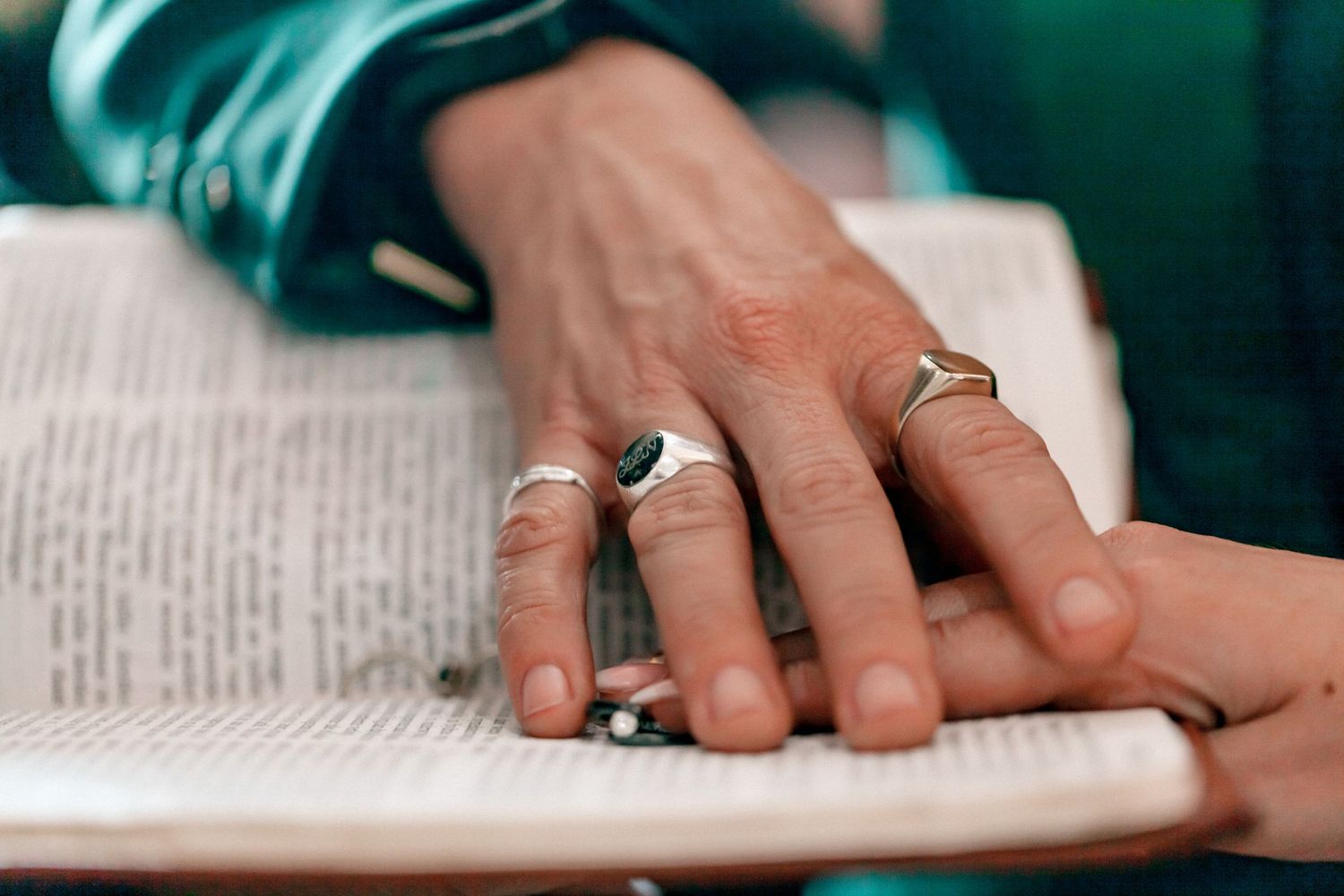 Close-up view of hands holding a pen while writing on paper in teal-tinted lighting.