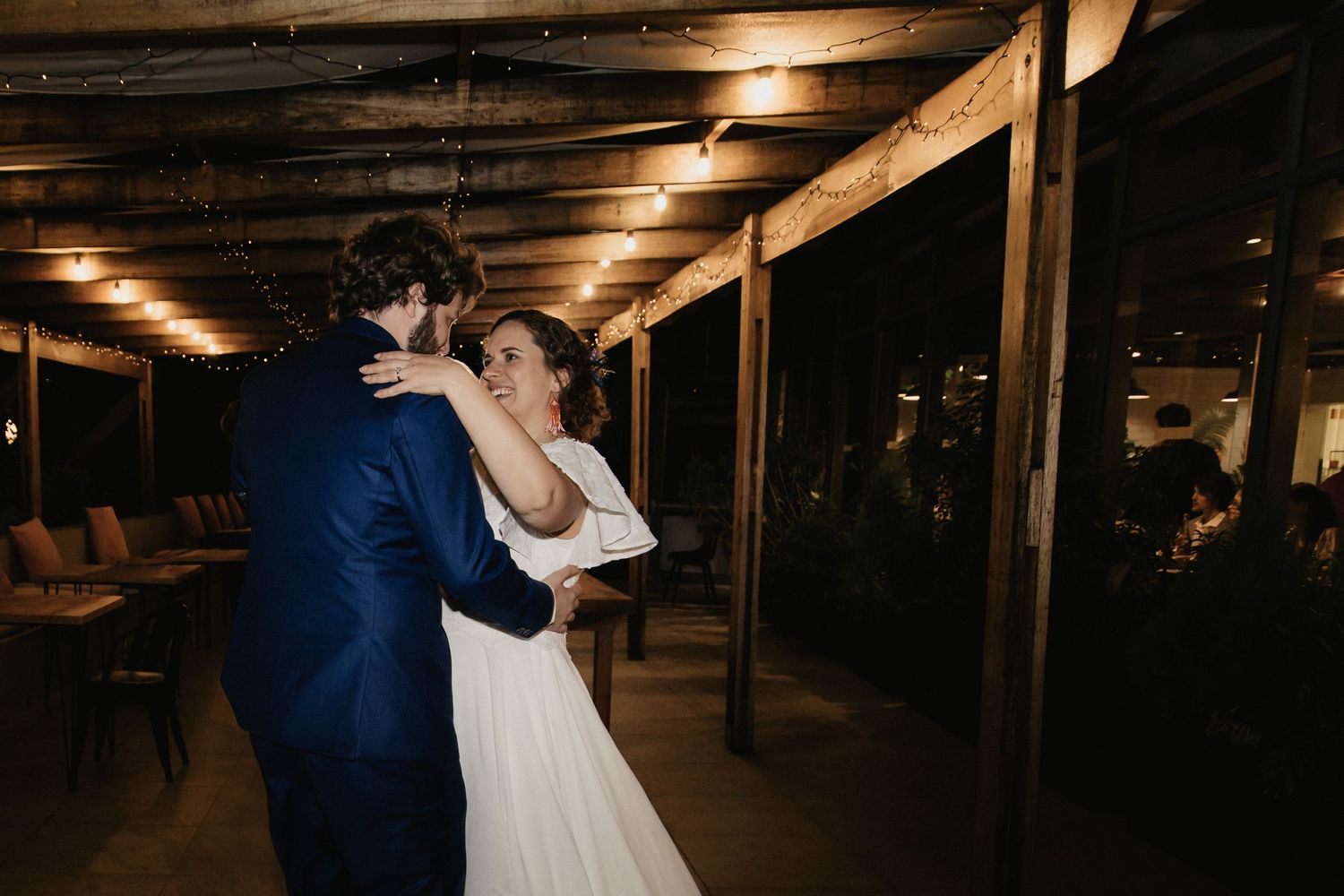 A romantic couple shares a tender dance moment in a dimly lit rustic venue with wooden beams overhead.