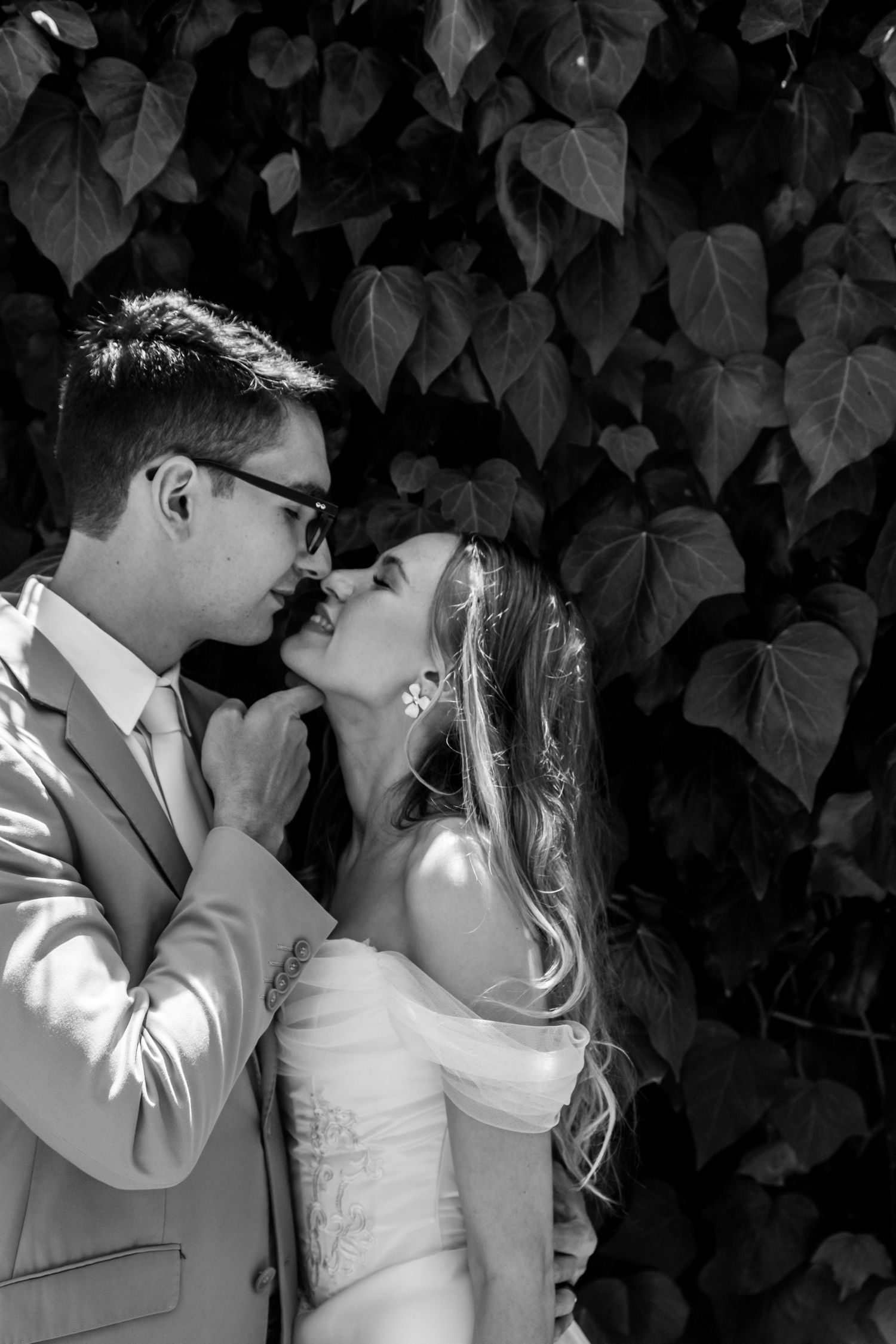 Black and white wedding photo sequence showing a romantic kiss between newlyweds against a leafy backdrop.