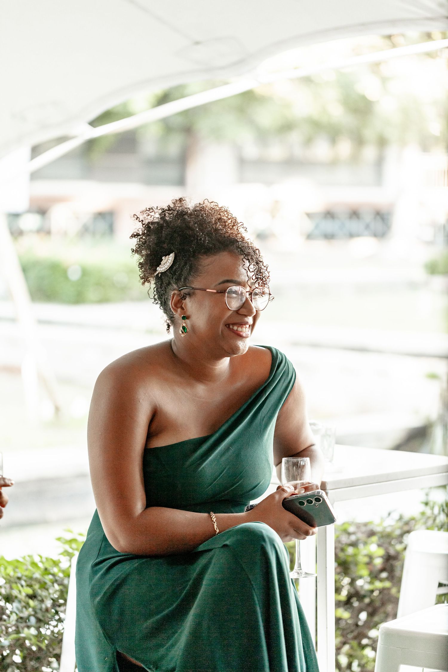 Person wearing a green one-shoulder dress laughs joyfully in an outdoor setting with bright natural lighting.