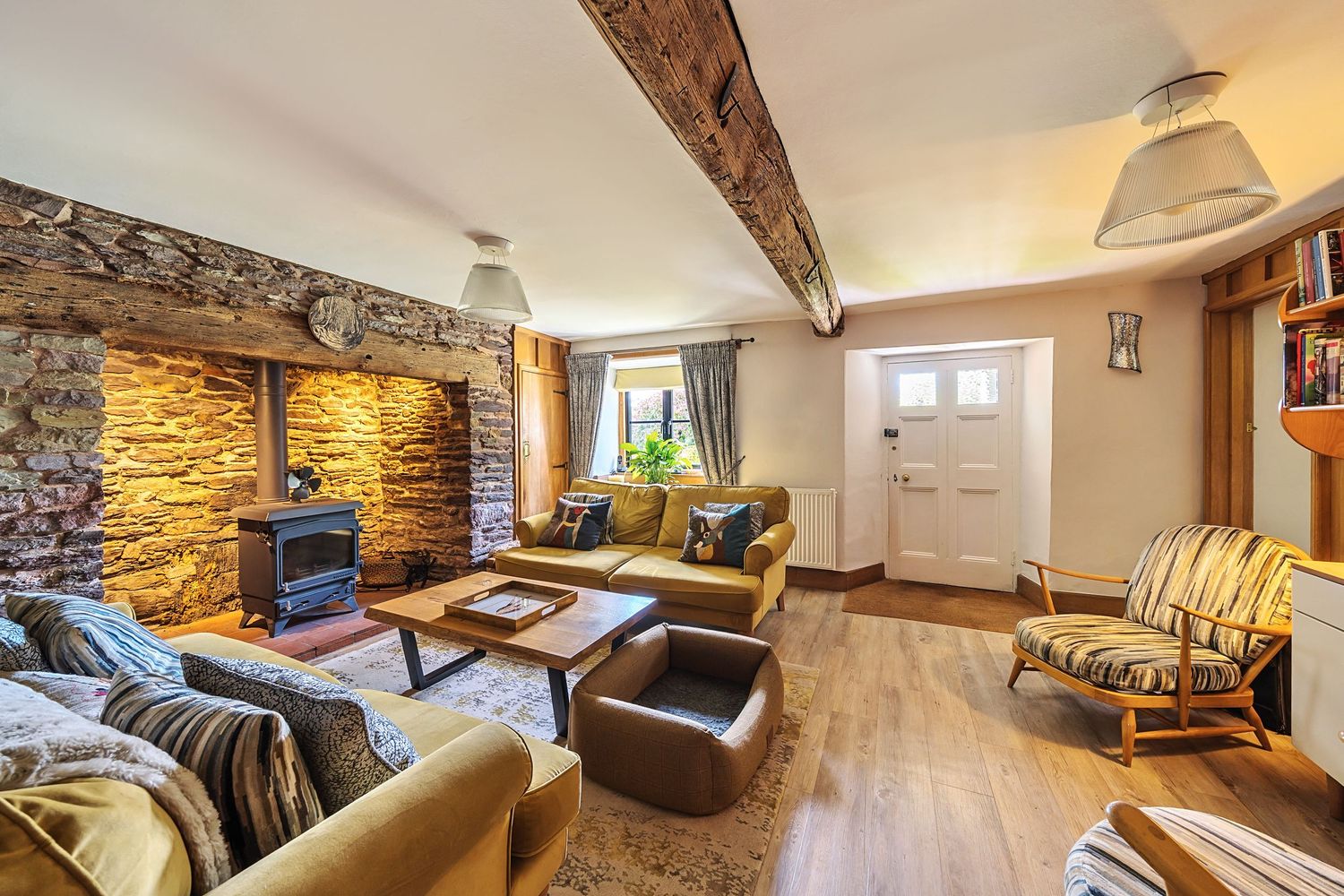 Cozy cottage living room with stone walls, exposed wooden beam, wood-burning stove, and comfortable leather sofas.