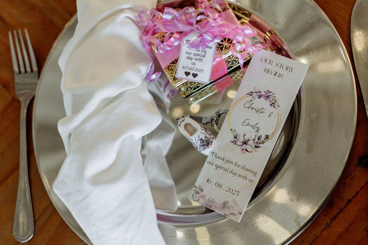 White china plates with pink floral gift tags and silver cutlery arranged on a rustic wooden surface.