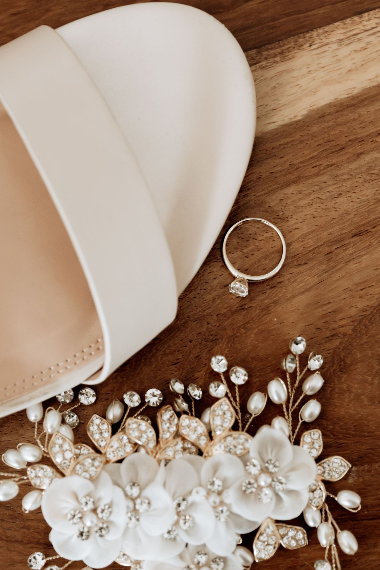 Wedding accessories including a pearl and crystal hair piece, engagement ring, and white handkerchief on wooden surface.