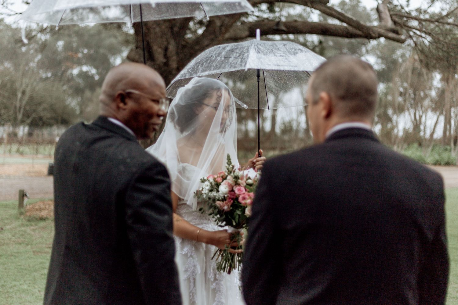 A couple shares an intimate moment under a clear umbrella in the rain during a romantic outdoor photoshoot.