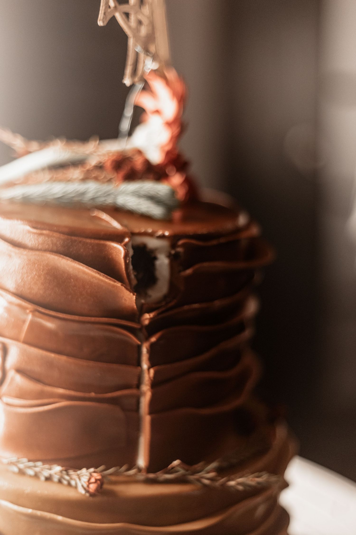 Close-up of a rustic chocolate cake with textured frosting and dripping layers in warm lighting.