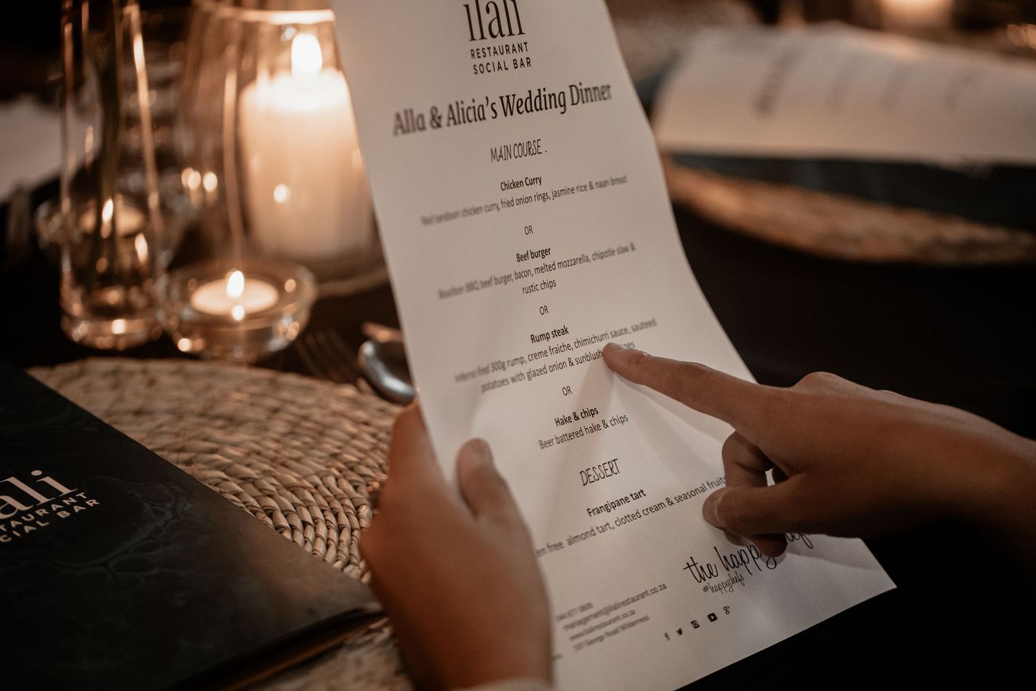 Hand holding an elegantly designed wedding menu in warm candlelit ambiance at an intimate reception setting.