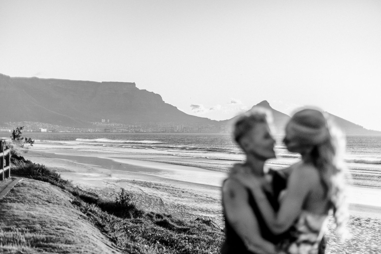 A couple embraces on a scenic coastal cliff overlooking a dramatic ocean landscape at sunset.