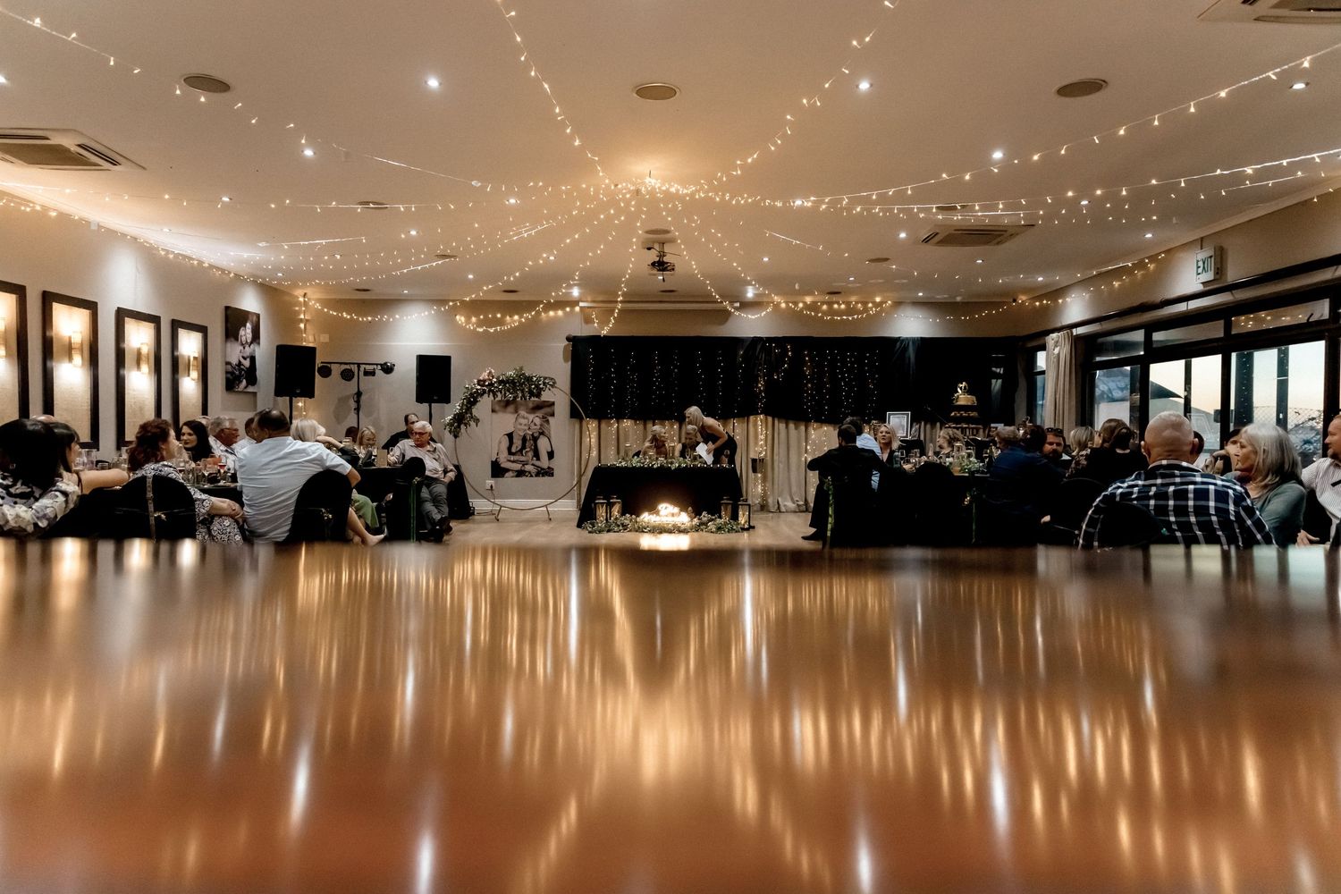 Large ballroom with wooden dance floor and string lights decorating the ceiling creates an elegant reception atmosphere.