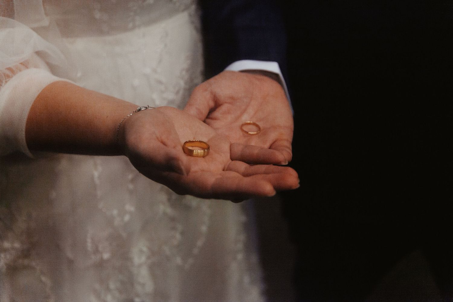 Close-up view of hands holding wedding rings against a dark background.