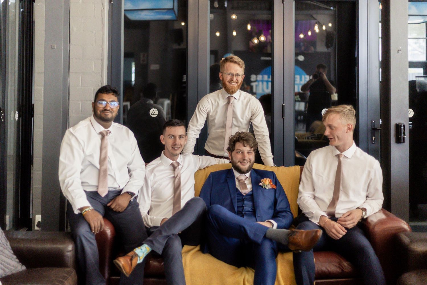 A group of people in formal attire pose together in a modern office setting with string lights in the background.
