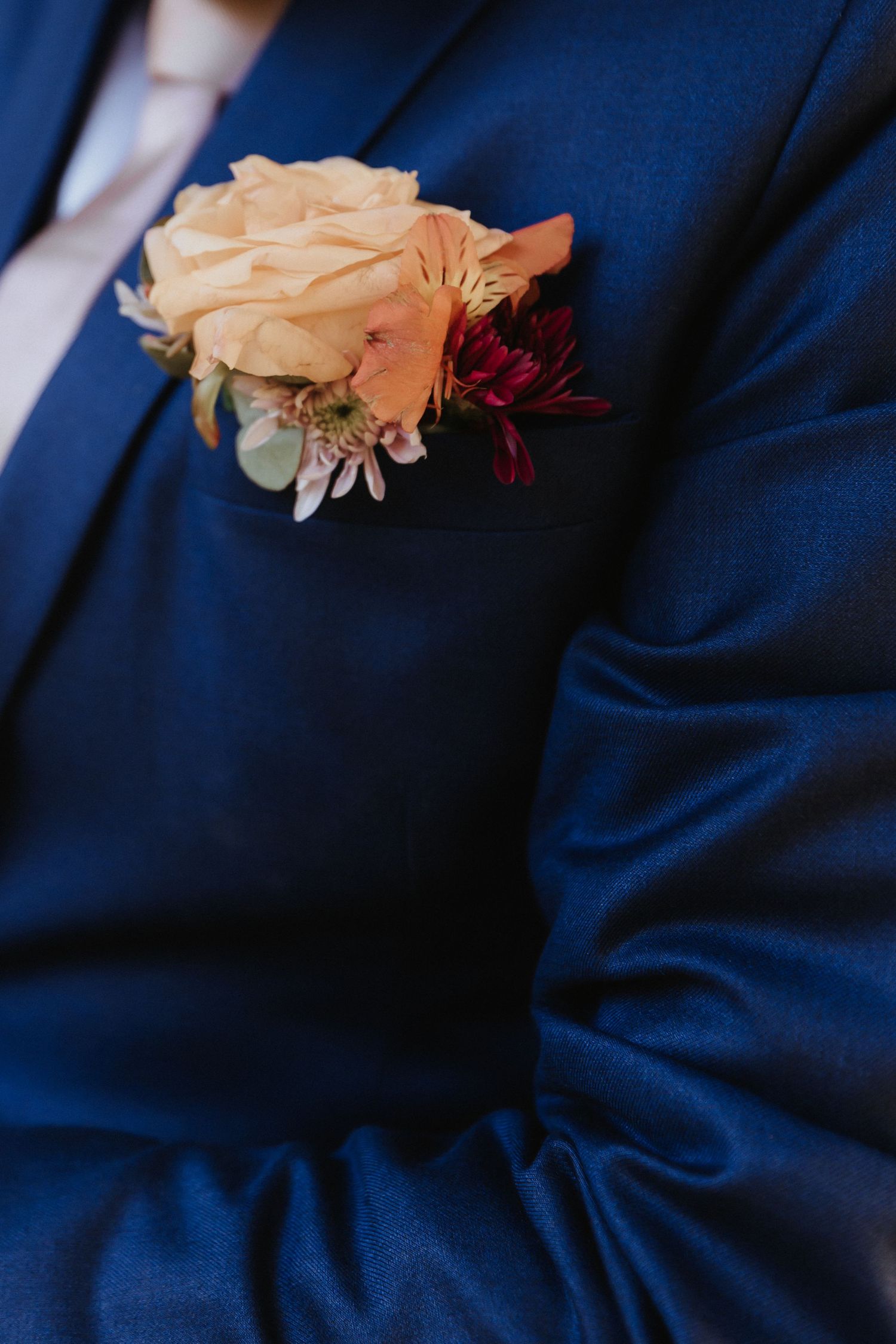 Peach and burgundy floral boutonniere against a dark navy blue suit fabric background.