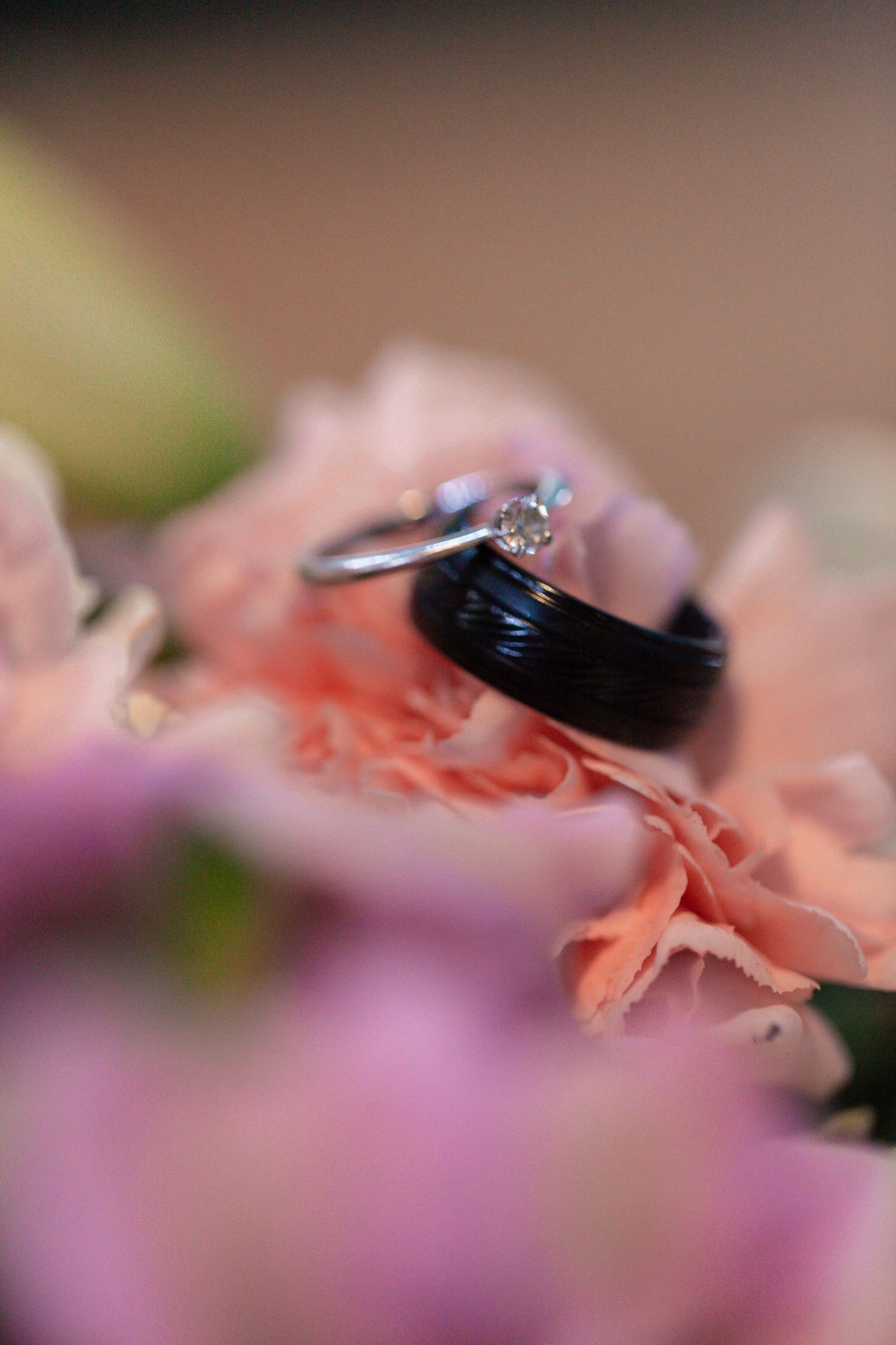 Close-up macro photograph of an engagement ring with pink and purple floral elements in soft focus.