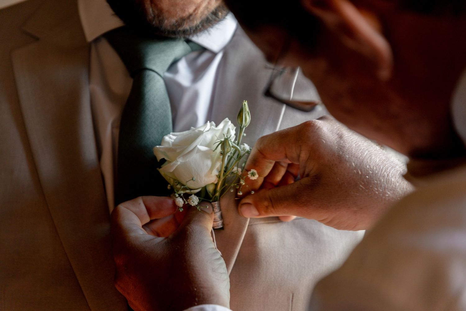 Groom getting a white rose boutonniere pinned to his suit lapel at a wedding ceremony.