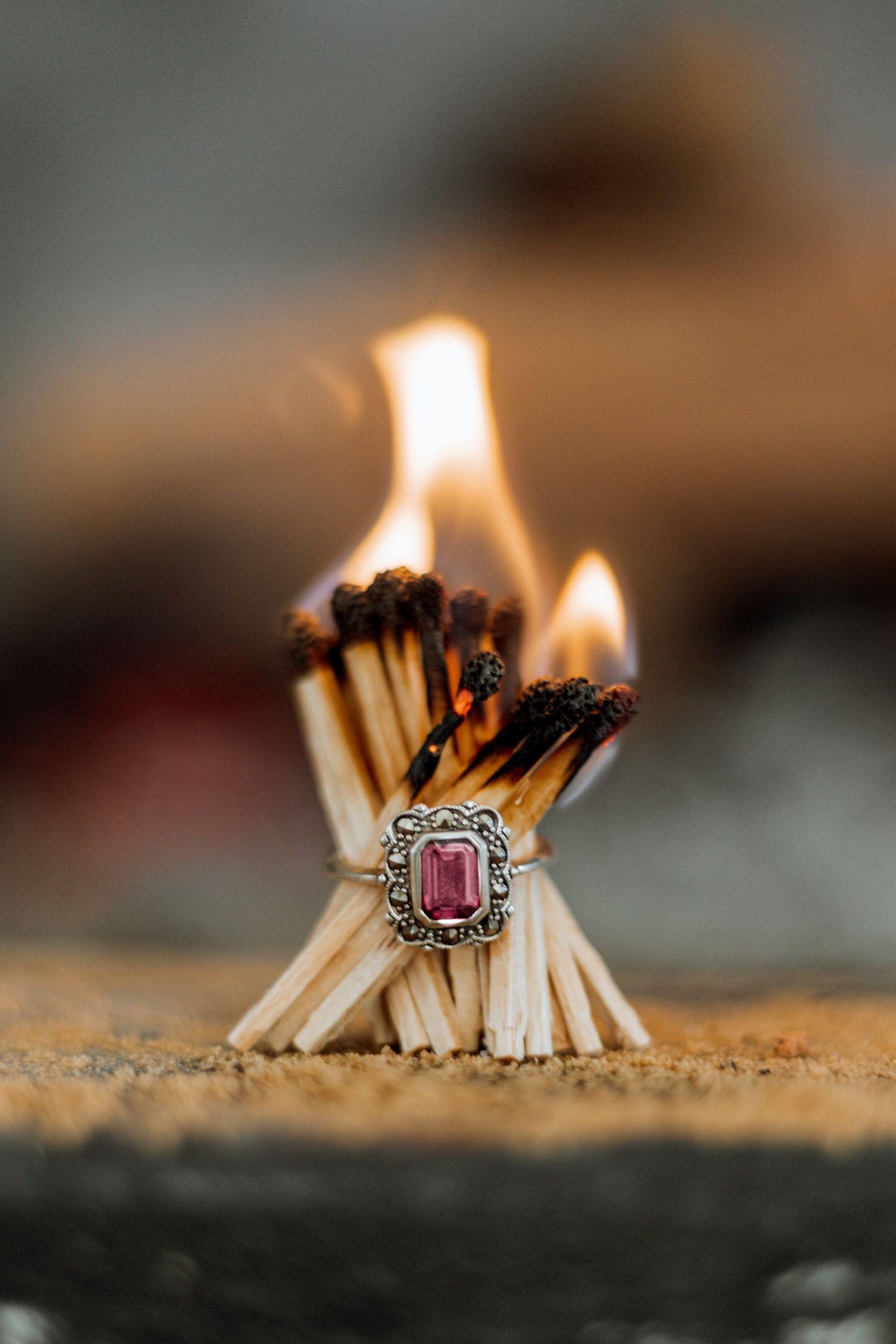 Artistic sequence showing matches burning in a row with a pink gemstone ring resting against them.