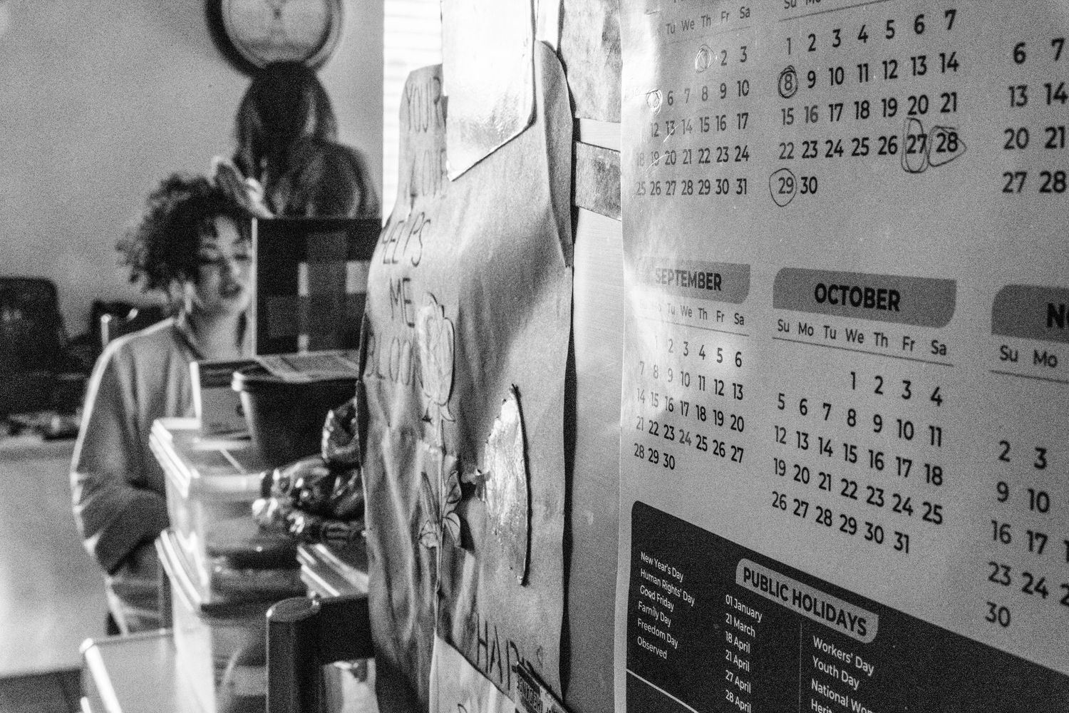 Vintage style black and white photo showing various calendar pages hanging on a wall.
